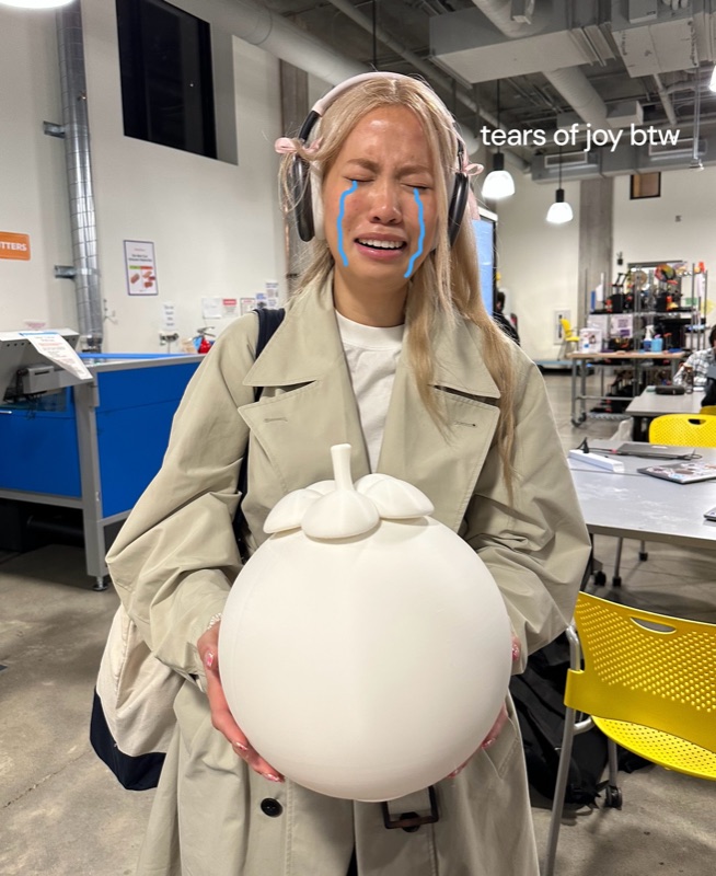 Cindy crying tears of joy, holding a large white 3D-printed mangosteen
